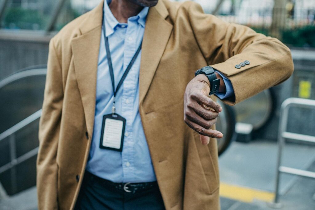 Crop anonymous African American businessman in elegant formal suit looking at wristwatch while standing near metro entrance