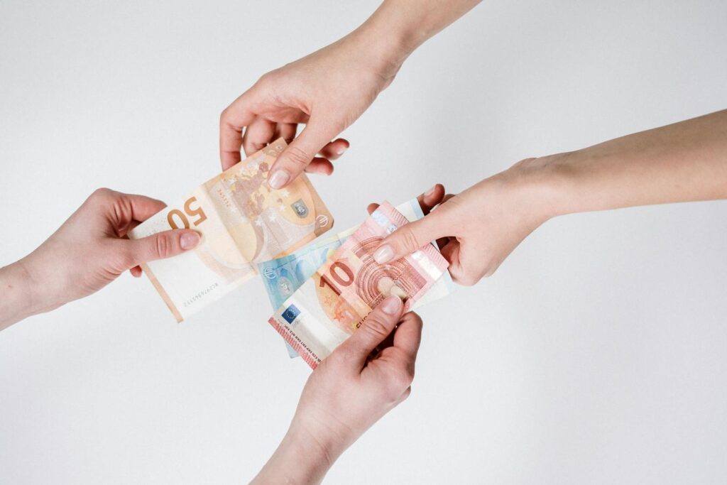 Two pairs of hands exchanging Euro banknotes, symbolizing finance and transaction.